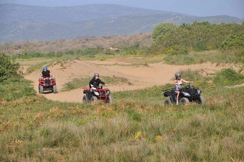 Three people riding ATVs on a dirt path in a grassy area with hills in the background. 4
