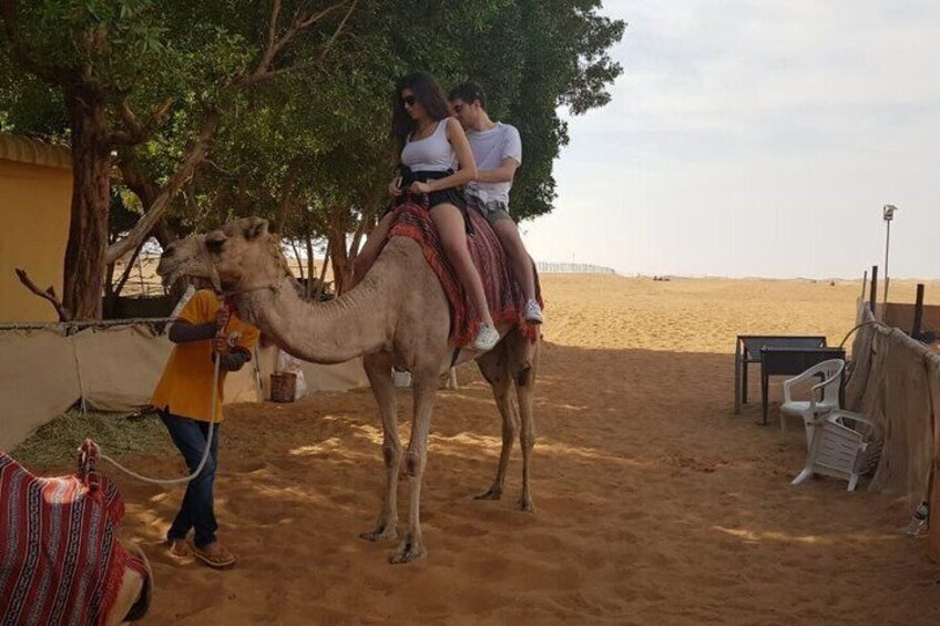 A camel with a person riding it, a person leading the camel, and a beach in the background. 3