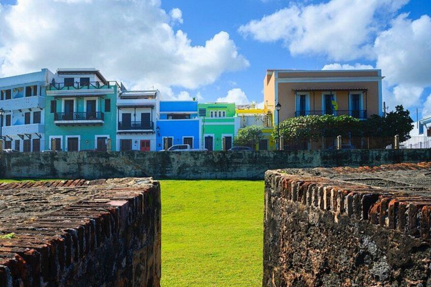 A coastal town with colorful buildings, a grassy area, and old stone walls. 2