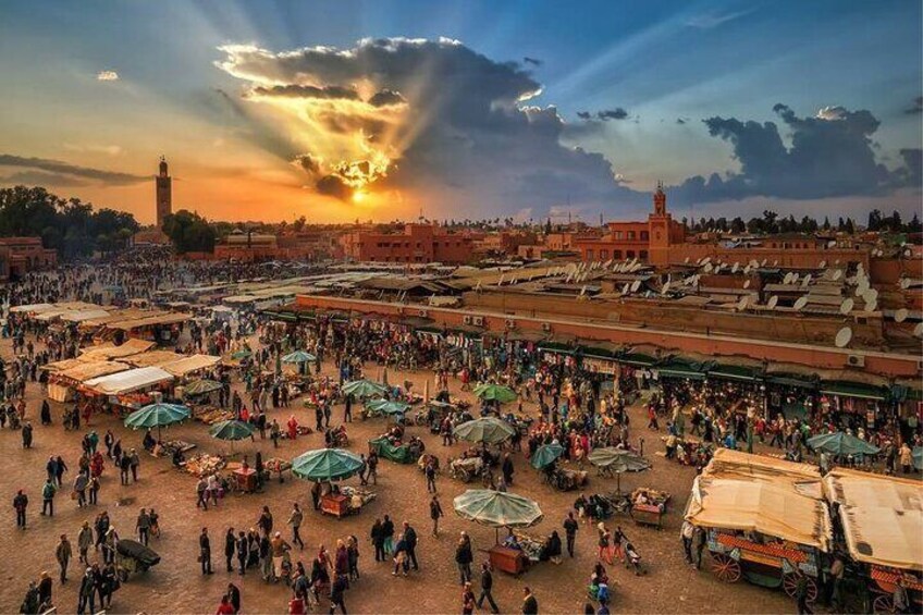 Un marché animé, où l’on peut voir des gens et des étals sous un ciel embrasé par le coucher du soleil. 1