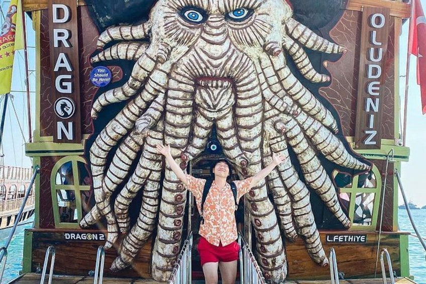 A person standing in front of a large octopus sculpture with the words 'DRAGON' and 'OLUDENIZ' on the sides. 2
