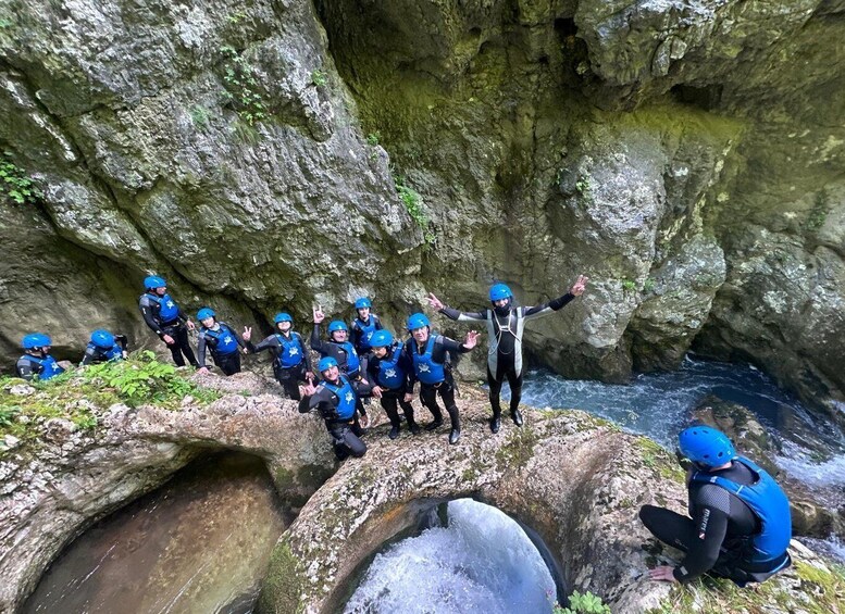 A group of people in blue helmets and wetsuits standing on rocks by a flowing river in a rocky gorge. 1