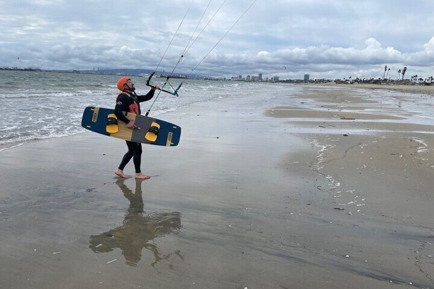 A person walking on a beach carrying a kiteboard. 4