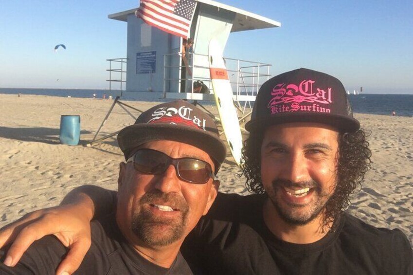 Two people wearing hats with text, a lifeguard tower, and a beach with a blue barrel. 2