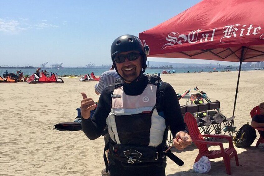 A person in a wetsuit and helmet on a beach with red umbrellas and kites in the background. 3