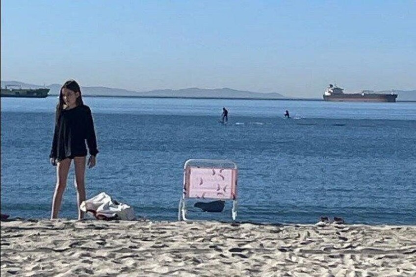 A beach with a person standing, a pink chair, and a ship in the distance. 4