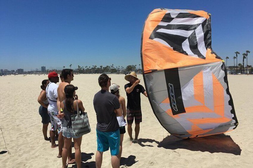 En gruppe mennesker på en sandstrand med en stor orange og sort drage. 4