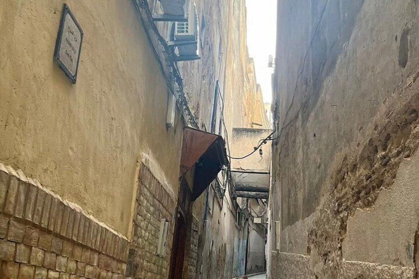 A narrow alleyway with old buildings, a hanging sign, and a brick wall. 3