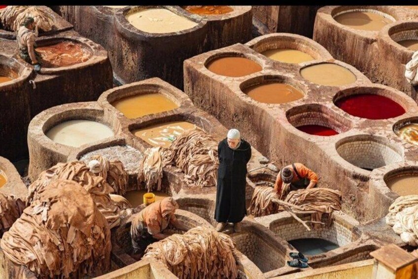A tannery with large stone vats of different colors, a person in black, and leather goods. 2