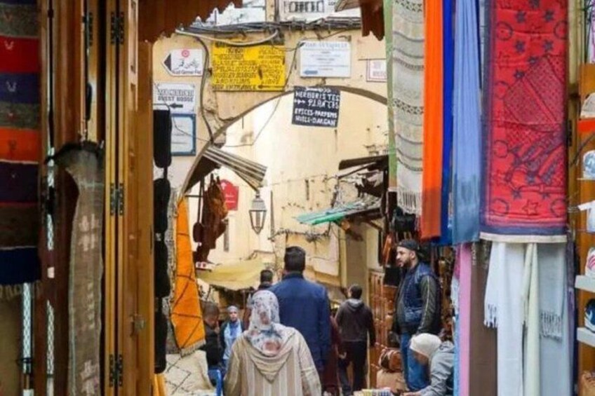 A crowded market street with people shopping and a signboard visible. 5