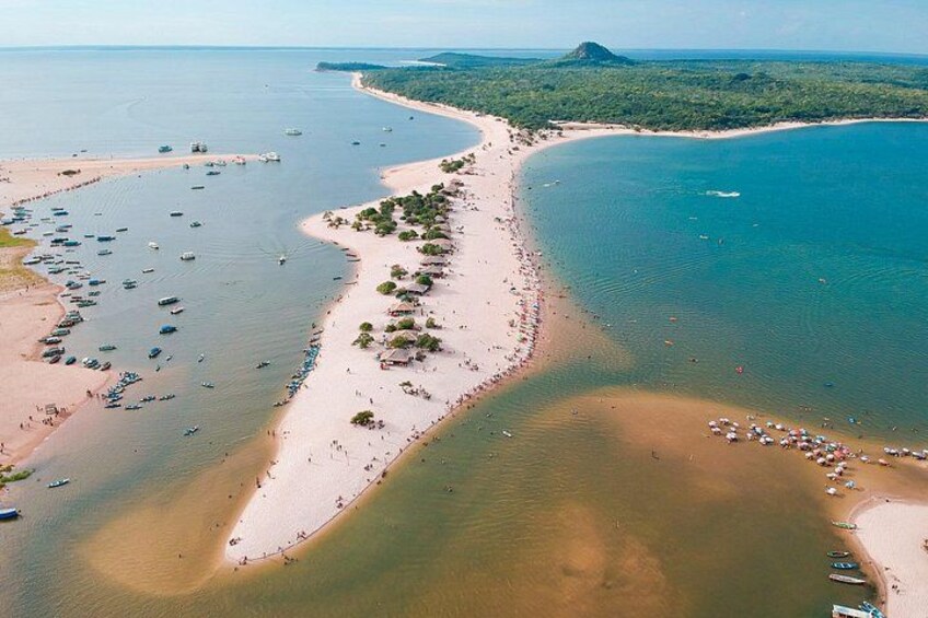 An aerial view of a coastal area with a sandy beach, calm waters, and a forested peninsula. 4