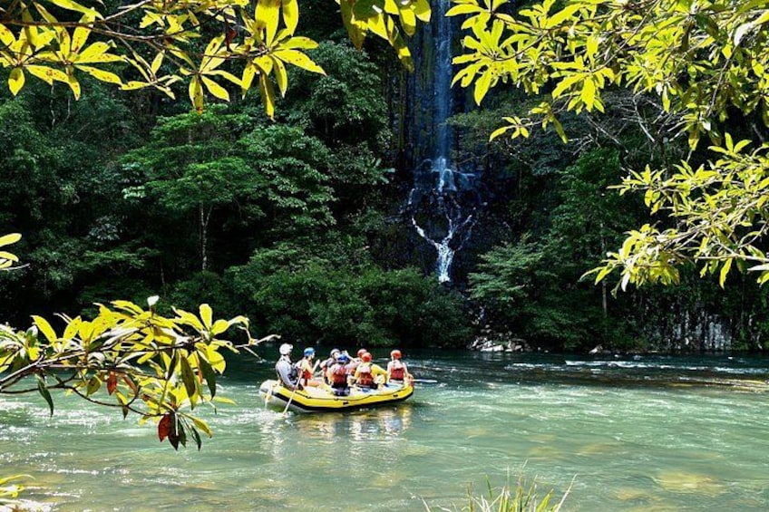 A group of people in a yellow raft on a river surrounded by dense green foliage and a waterfall. 3
