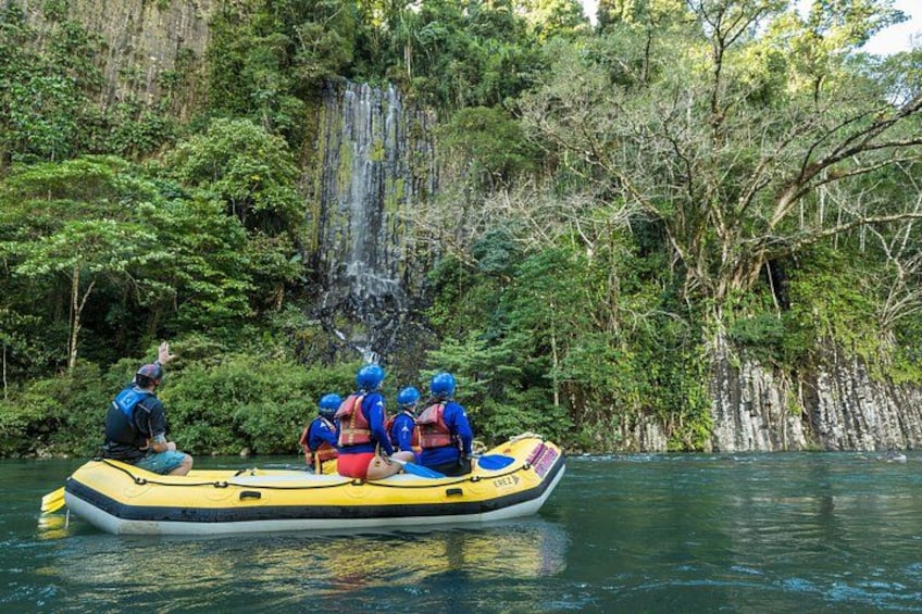 A group of people in a yellow raft on a river surrounded by dense forest and a waterfall. 4