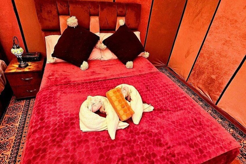 A red velvet bed with two pillows, a white blanket, and a stuffed animal. 2