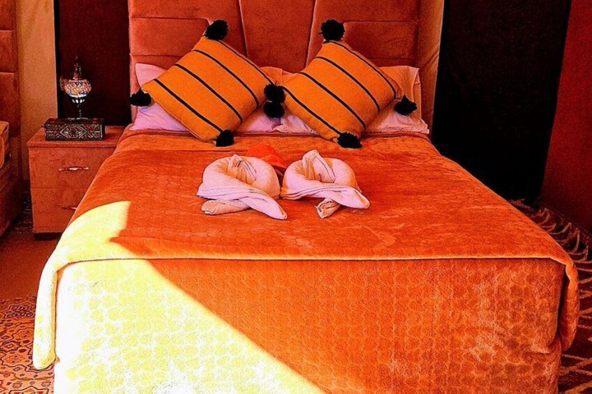 A bed with an orange bedspread, two pillows, and a folded towel on the bed. 4