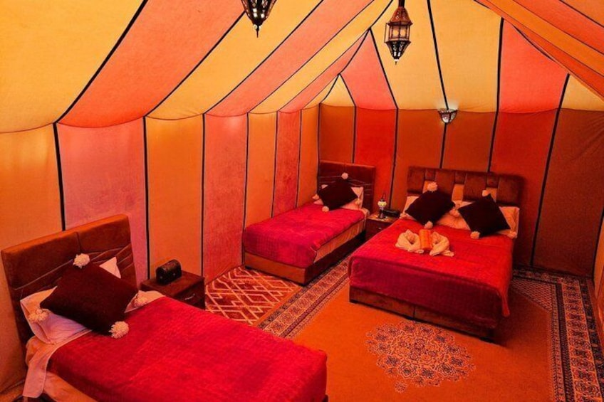 A tent with two beds, each with red bedding and pillows, and a patterned rug on the floor. 5