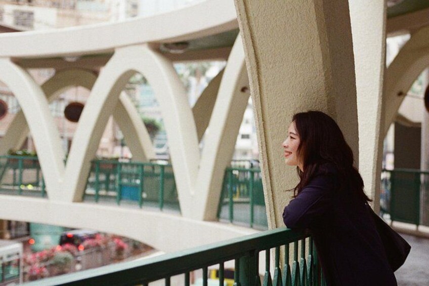 A person leaning on a white structure with green railings, overlooking a plaza with plants and a building in the background. 4