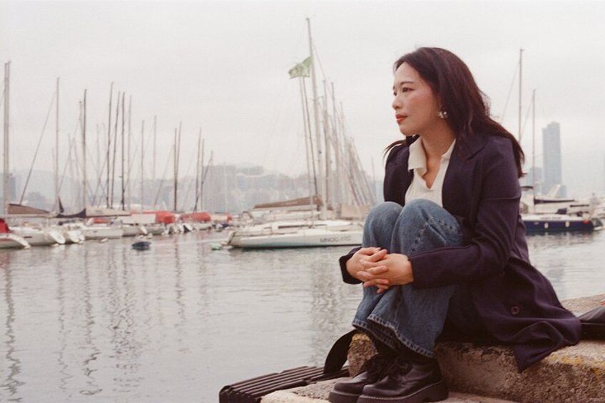 A person sitting on a concrete ledge by a marina with boats in the background. 2