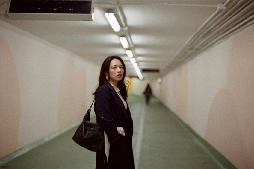 A person standing in a hallway with fluorescent lighting, green walls, and a white ceiling. 3