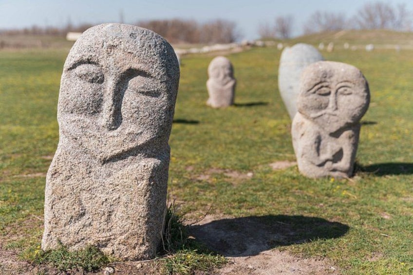 A stone head monument in a grassy field with other similar monuments in the background. 1