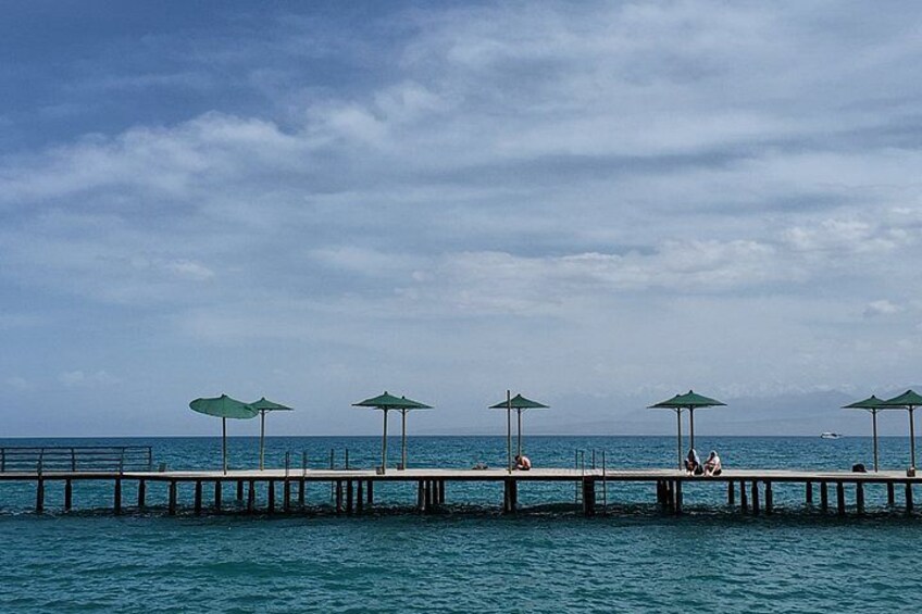 A pier with green umbrellas, calm water, and a clear sky. 3
