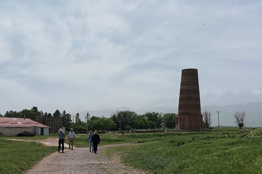 A tall, narrow tower in a grassy field with a few people walking nearby. 5