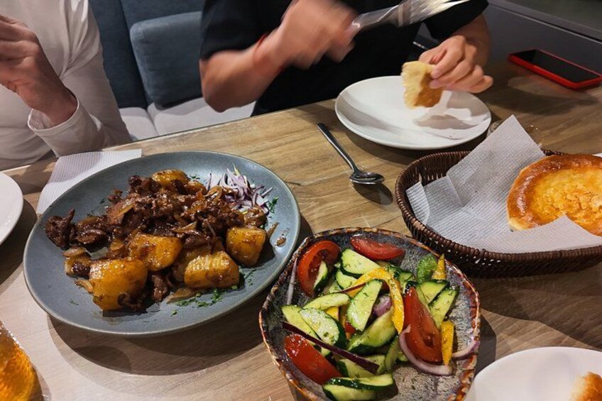 A dining table with various dishes including a plate of meat, a salad, and a basket with bread. 4