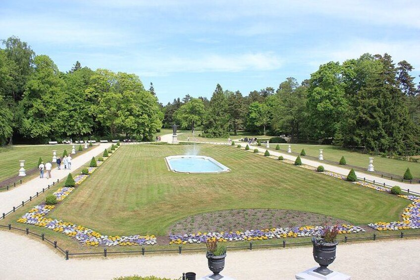A well-manicured garden with a central lawn, a fountain, and a variety of flower beds. 3