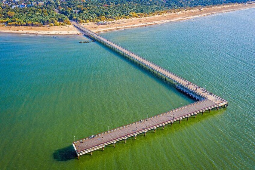 A long pier extending into a body of water, surrounded by greenery and a beach. 2