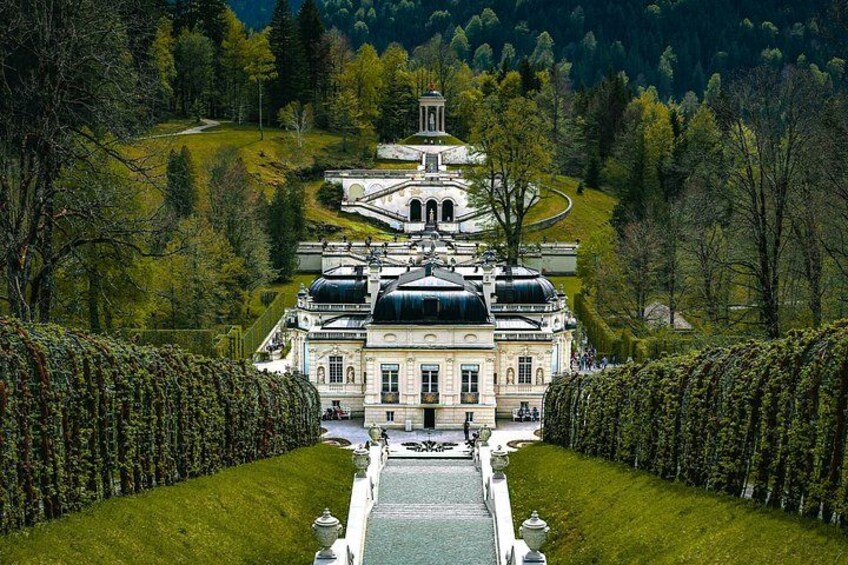 A grand estate with a central building, surrounded by manicured gardens and a formal pathway leading to it. 2