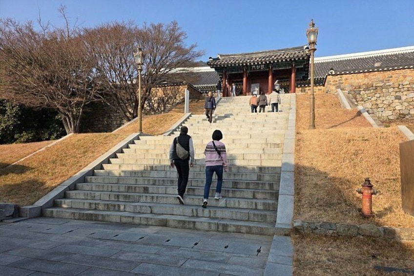 A stone staircase leading to a traditional building with a tiled roof, surrounded by dry grass and trees. 5