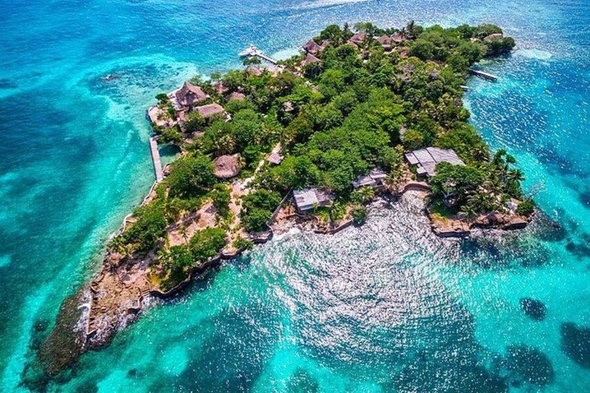 An aerial view of a tropical island with clear turquoise waters, lush greenery, and scattered structures. 3