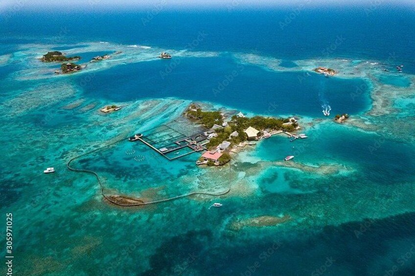An aerial view of a tropical island with clear turquoise waters, a small settlement with buildings, and a dock. 4