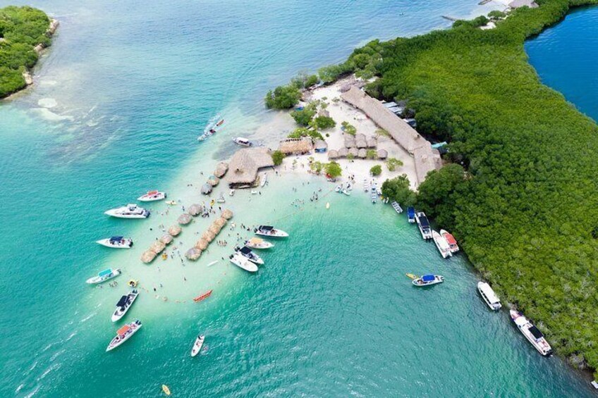 An aerial view of a tropical island with clear turquoise waters, a sandy beach, and several boats anchored near the shore. 2