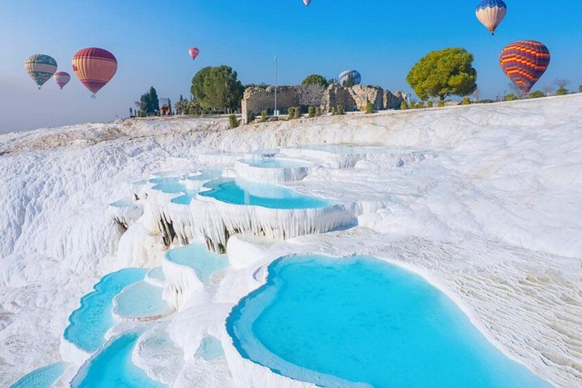 Terraced pools of turquoise water, white travertine formations, and hot air balloons in the background. 5