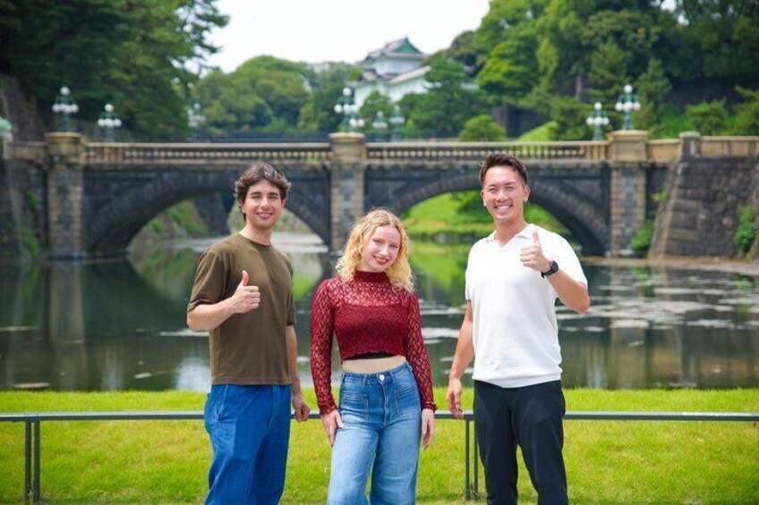 Three people standing in front of a stone bridge over a river with greenery in the background. 2