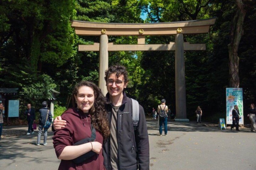 Due persone in piedi di fronte a un grande torii con uno sfondo boschivo. 5