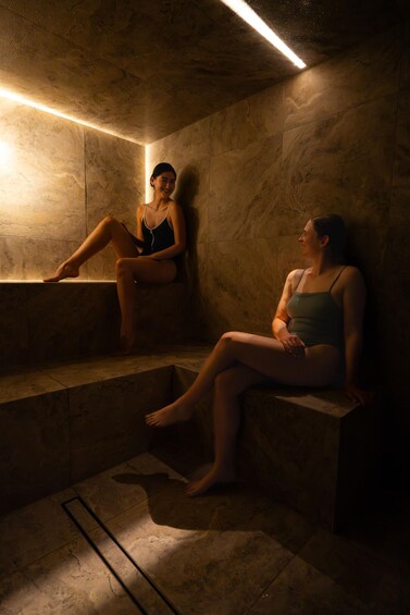 Two individuals seated on stone steps in a dimly lit room with a single overhead light. 1