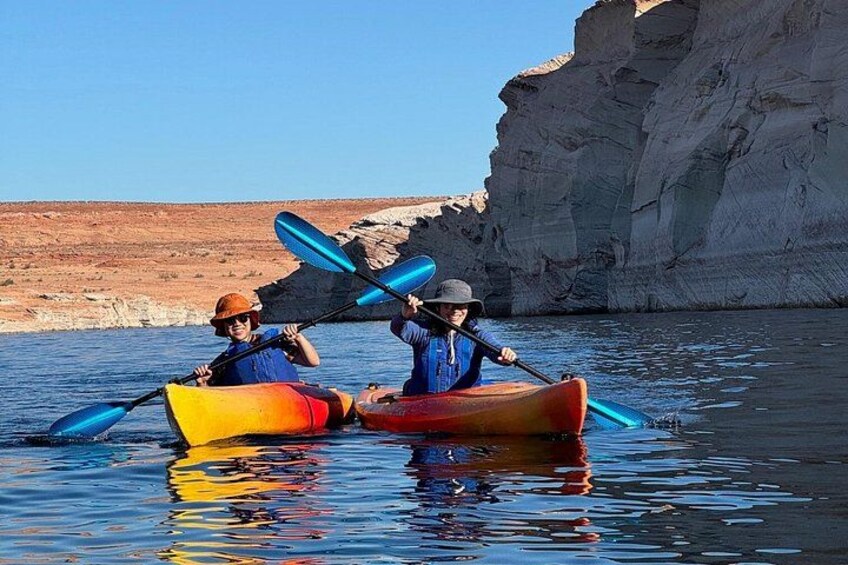 Two people kayaking on calm water with cliffs in the background. 2