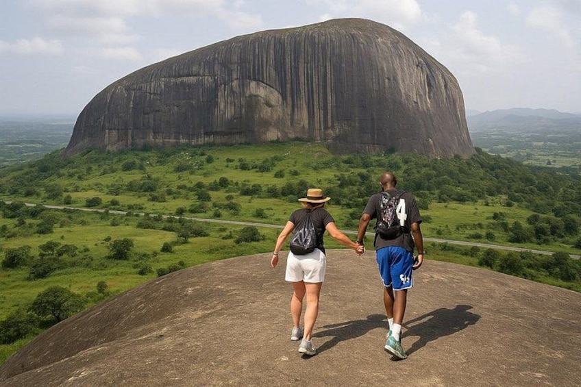 Two people walking on a large rock formation with a large natural rock structure in the background. 1