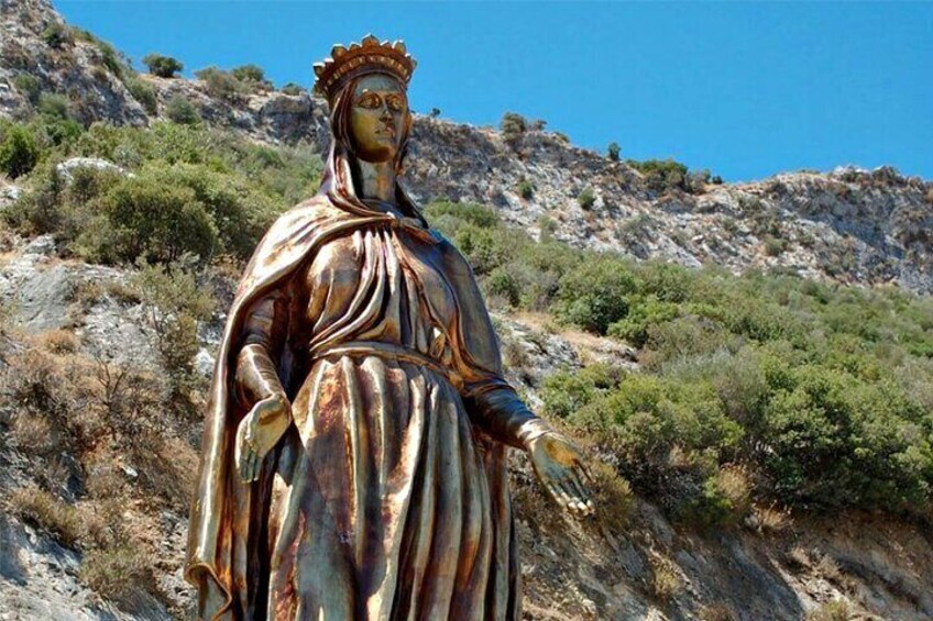 A statue of a robed figure with a halo, standing on a rocky hillside with sparse vegetation. 1