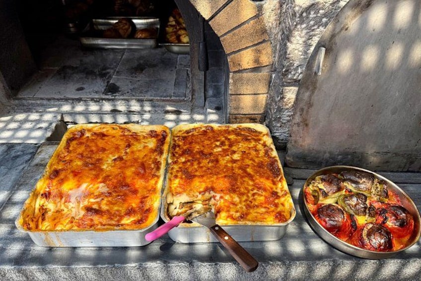 Two rectangular metal trays with baked food, a pizza peel, and a pan with roasted vegetables. 4
