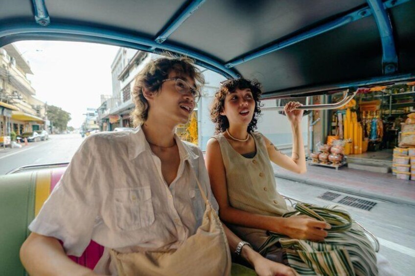 Two people in a vehicle, one holding a plant, with buildings and a street visible through the window. 3