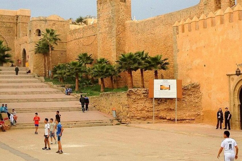 A historical site with stone walls, palm trees, and people walking. 3