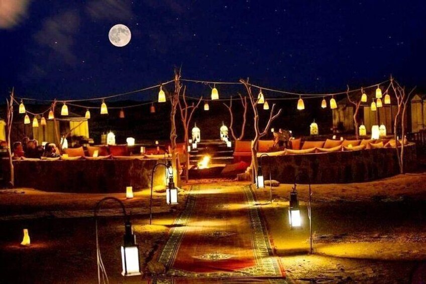 A nighttime outdoor seating area with string lights and lanterns, a pathway, and a moon in the sky. 3