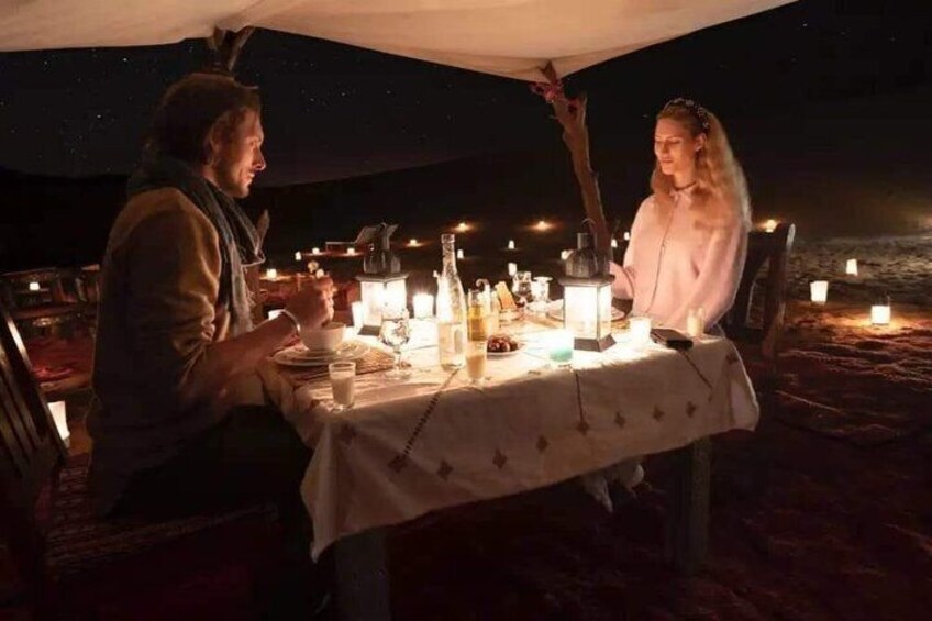 A couple dining at a beachside table under a canopy, with candles and a lantern providing light. 2