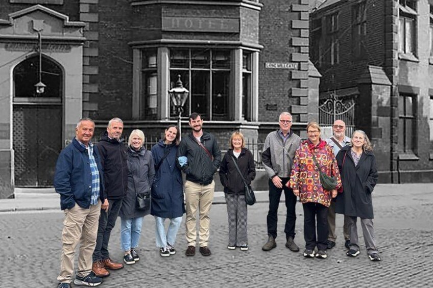 Eine Gruppe von Personen steht vor einem Gebäude, an dem ein Schild mit der Aufschrift 'HOTEL' zu sehen ist. 2