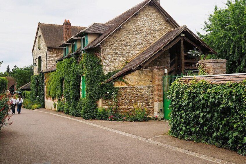 A stone building with ivy, a paved road, and a hedge. 3