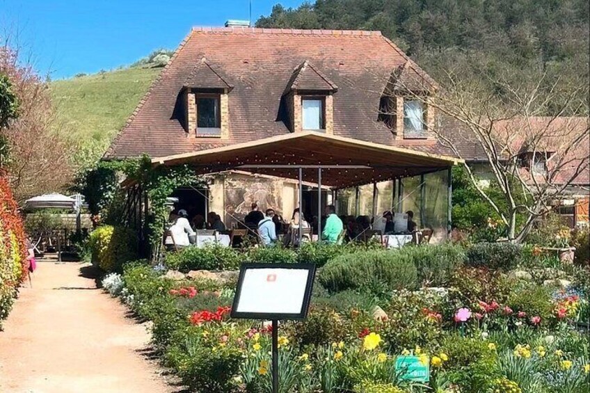 A rustic building with a covered patio, surrounded by a garden with various flowers and a dirt path leading to it. 4