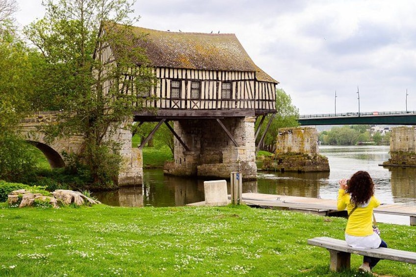 Un edificio histórico con entramado de madera, un puente, un río y una persona sentada en un banco. 5